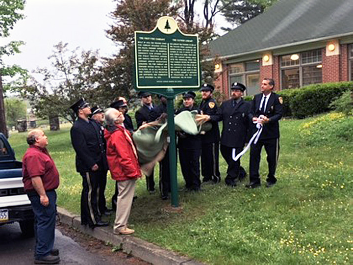 Fire company members unveil the marker, located outside the Clymer Library.
